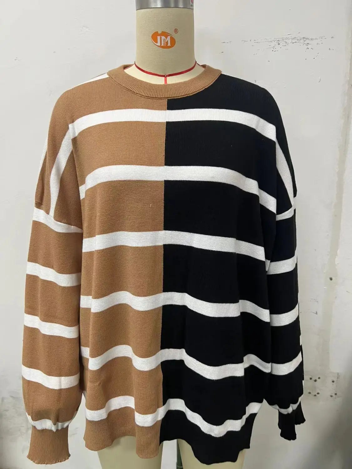 A cozy women’s oversized knit sweater featuring a bold two-tone split color design in warm tan and black with crisp white horizontal stripes across both sides.