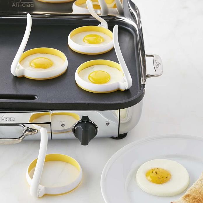 Silikon-Eierring für eine runde Omelettform mit Griff in Weiß und Gelb, mit flexiblen Griffen für die perfekte Zubereitung gleichmäßig runder Spiegeleier auf einer Grillplatte.