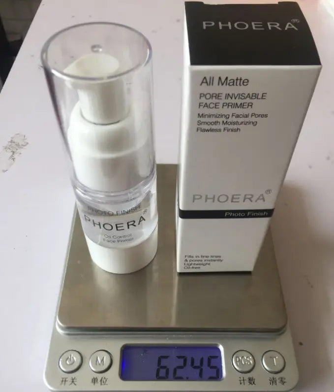 white Phoera matte pore invisible face primer in a clear pump bottle with white accents displayed next to its matching box on a digital scale for precise measurement