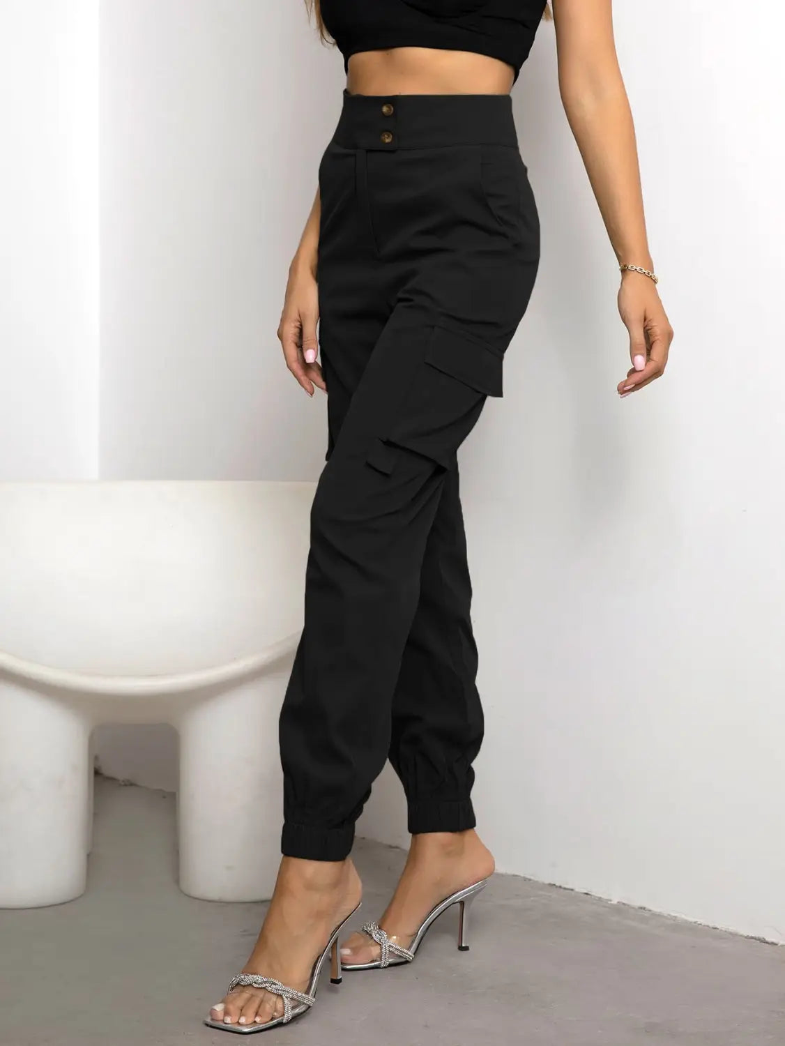 Pantalon cargo noir taille haute pour femmes en polyester, avec jambes fuselées, fermetures à boutons et ourlets boutonnés.