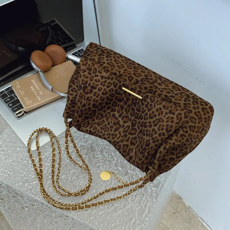 Brown leopard print crossbody bag with a gold tone chain strap and a matching circular charm.