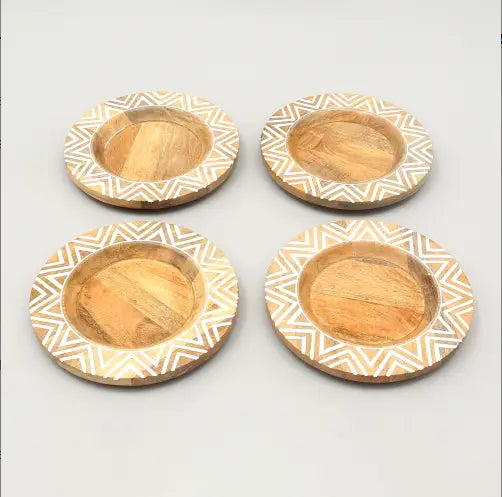 Lot de quatre dessous-de-plat circulaires en bois, avec une finition claire en bois naturel et des motifs d’incrustations géométriques blanches complexes le long du bord, provenant de l’ensemble de table en assiettes plates en bois rustique fait à la main.