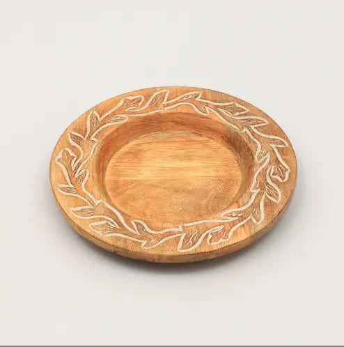 Une assiette plate ronde en bois, avec une finition brun clair naturelle et un motif de couronne de feuilles gravé le long de son bord, fabriquée dans un style rustique pour un usage en table.