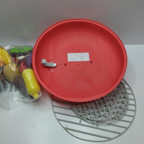 Back side of a red plastic circular smoking barbecue grill toy with light and sound features, silver metal handle, and white label on the underside.