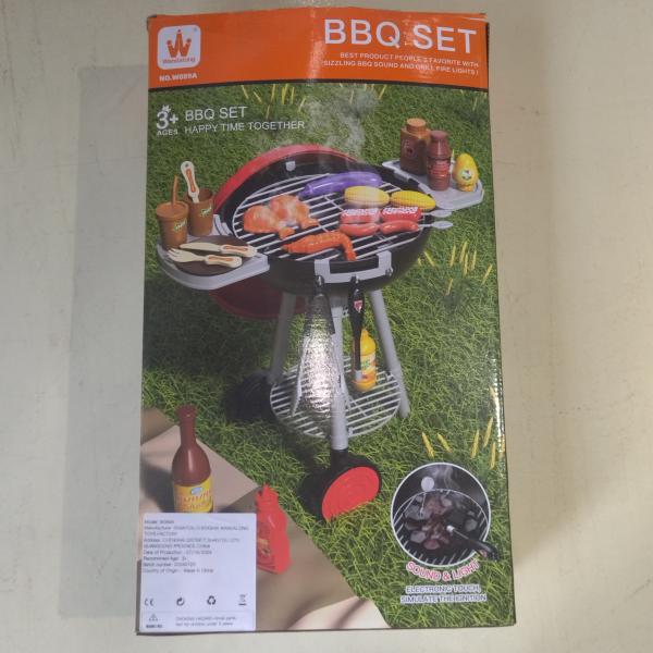 Red and black plastic smoking barbecue grill toy with light and sound features, wheels, grilling surface, side shelves for condiments and food items, and an attached lower rack.