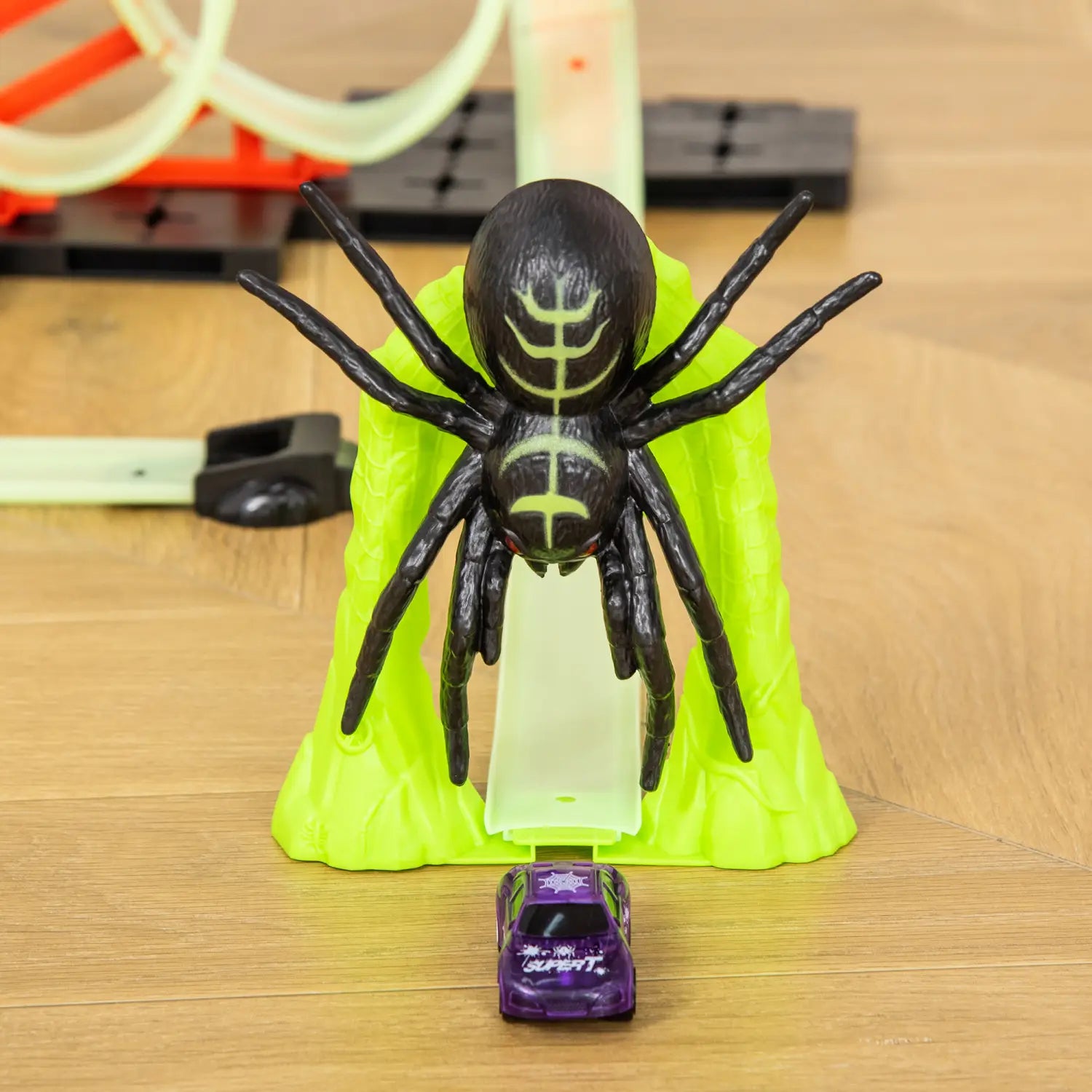 une araignée en plastique noir avec des marquages verts lumineux sur le corps et les pattes, placée sur une base vert citron vif, dans un circuit de course jouet araignée avec boucle pour jouer avec une voiture.