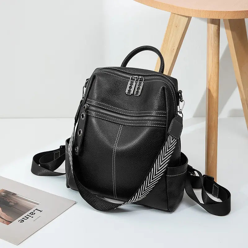 Black leather urban faux leather backpack with silver zippers and a contrasting black and white herringbone patterned shoulder strap.