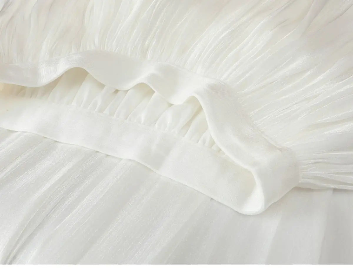 Jupe plissée délicate en mousseline de chiffon irisée blanche, avec une bordure à volants souples et fluides.