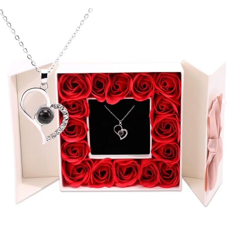 Silver heart-shaped pendant necklace with black spherical charm and embedded crystals displayed in an open gift box surrounded by red roses as part of the projection heart necklace and rose gift box set.