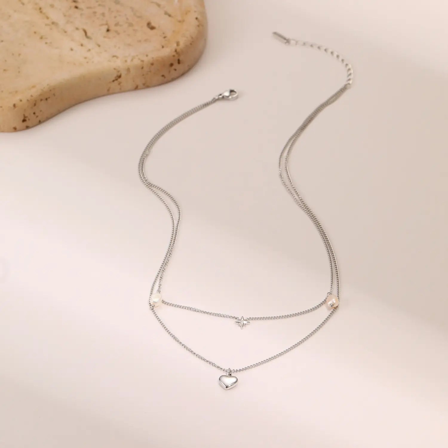 Silver double-layered stainless steel necklace featuring delicate chains with a small heart pendant, star charm, and tiny pearl-like beads, inspired by the double layer 18k gold star and pearl design.