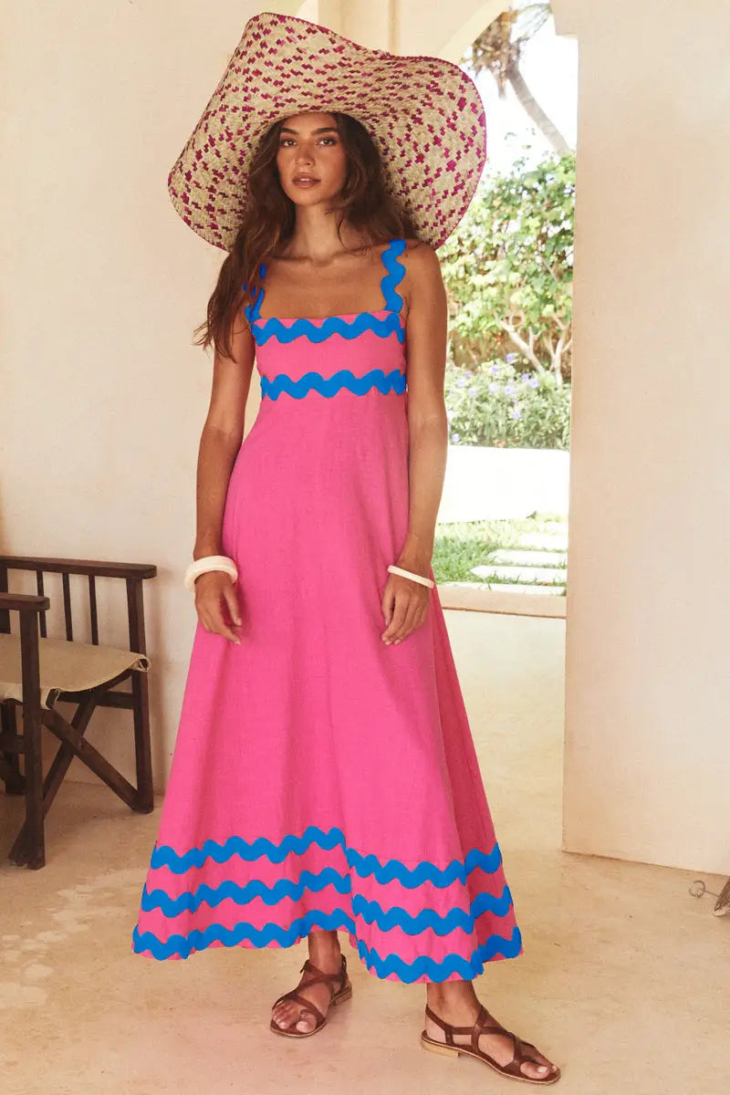 Un vibrante vestido maxi de playa floral con dobladillo ondulado, corte A, rosa, con ribete zigzag azul intenso a lo largo del escote y el bajo, y que presenta una silueta fluida.