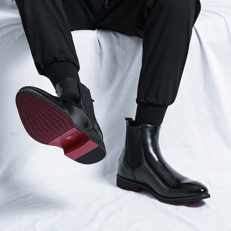 Men’s black patent leather Chelsea boots with a pointed toe and glossy finish featuring contrasting red soles.