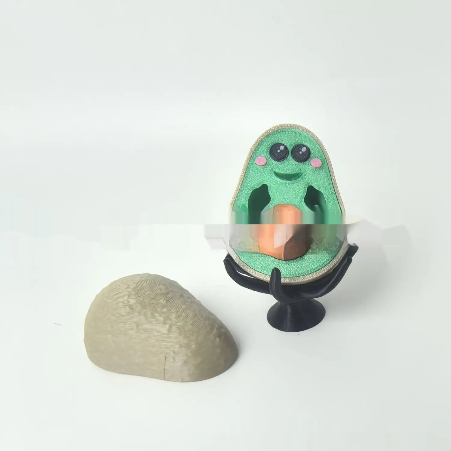 A charming green avocado-shaped soap dispenser with black eyes pink cheeks and a smiling face designed as a 3d printed desk toy phone stand measuring 6.5cm.