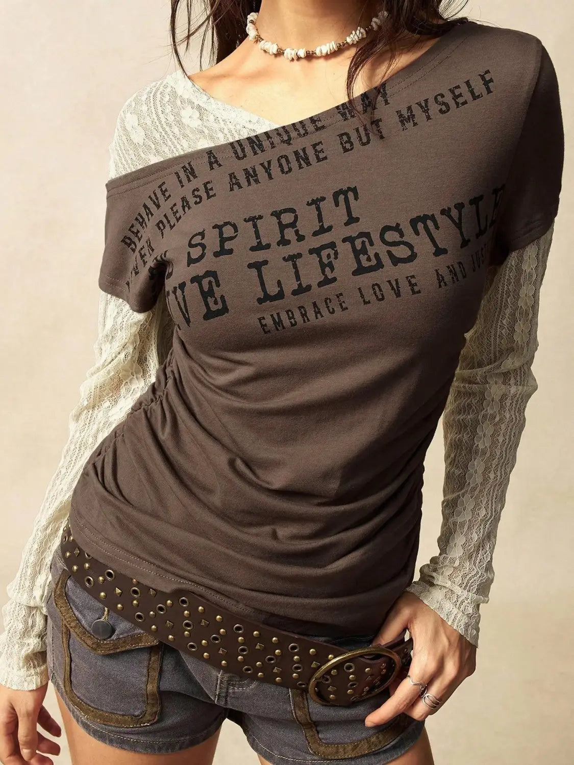 Brown lace layer off shoulder knitted top featuring a graphic tee design with layered lace sleeves and dark green inspirational text printed on the front.