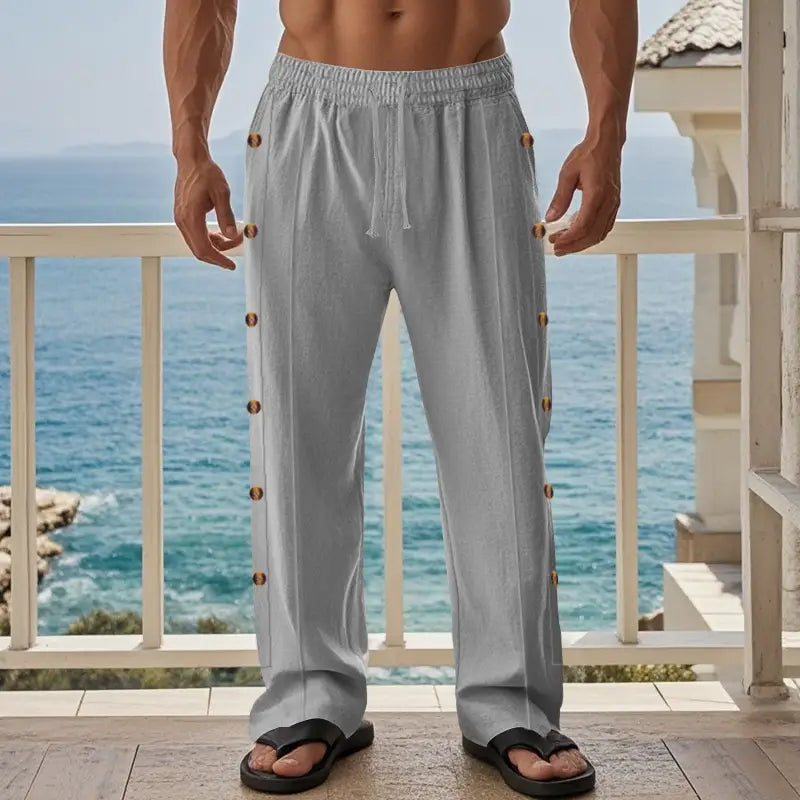 Light gray men’s linen straight leg pants with loose fit and gold toned side button detail down each leg.