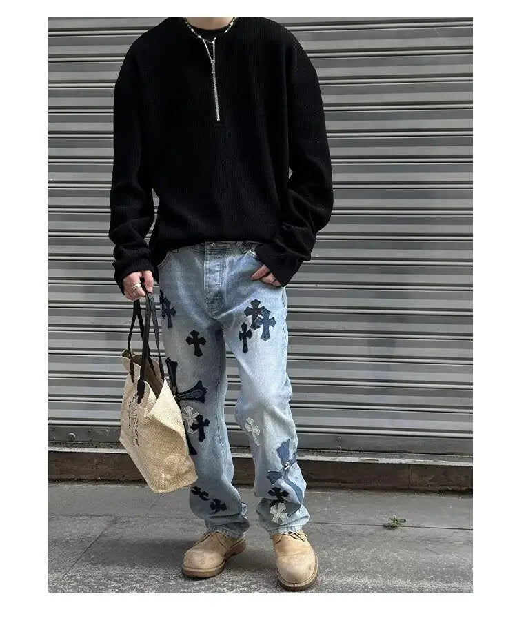 Sudadera tipo jersey acanalada de media cremallera para hombre combinada con jeans de mezclilla de lavado claro que presentan cruces bordadas en negro y blanco.