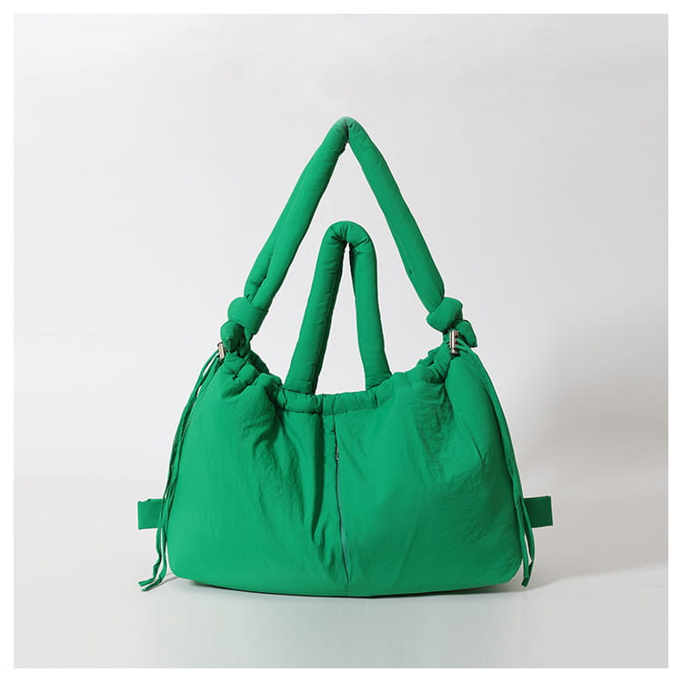 Vibrant green quilted puffer tote bag made of lightweight nylon with thick knotted handles and adjustable side straps for shoulder use.