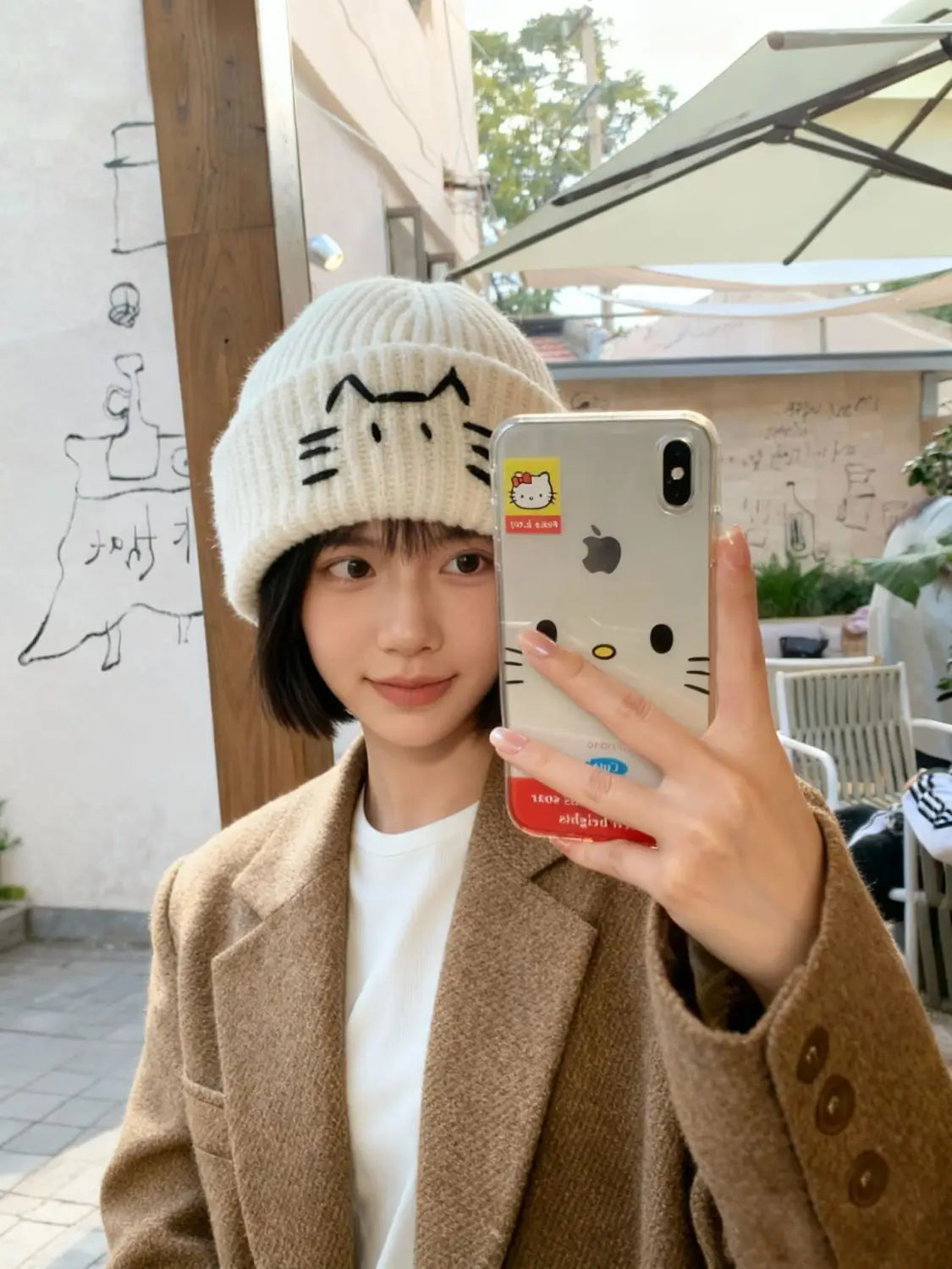 White knitted beanie hat featuring a black embroidered cat face design suitable for casual wear