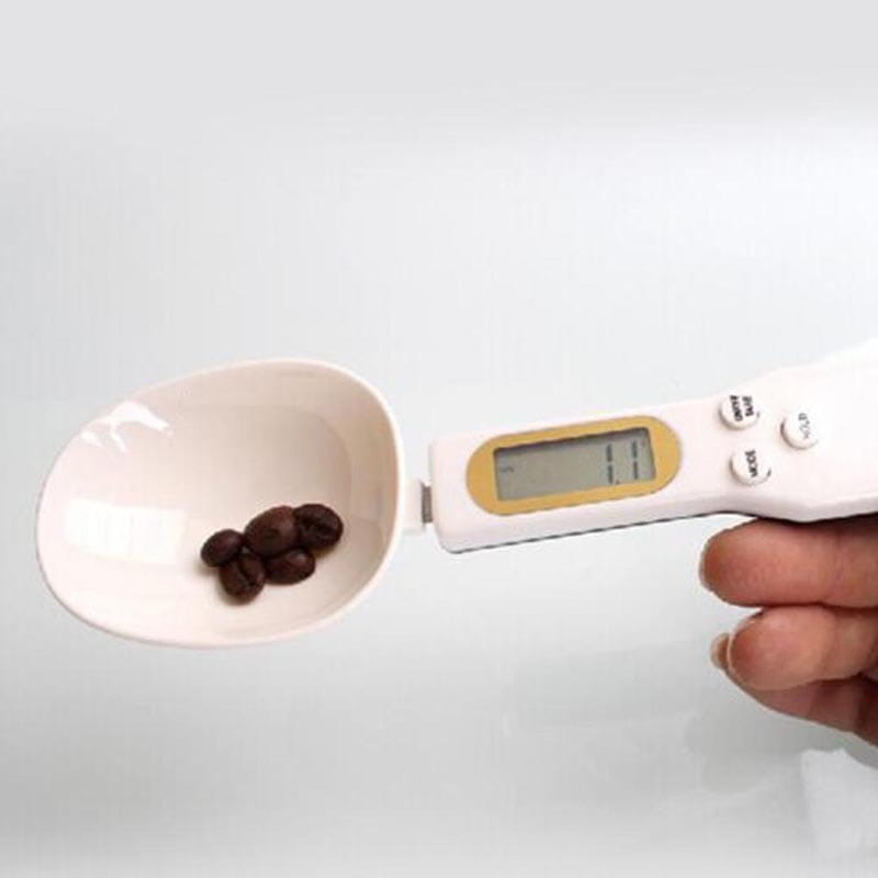 White digital spoon scale with lcd screen and buttons holding dark brown coffee beans for precise kitchen measuring up to 500g