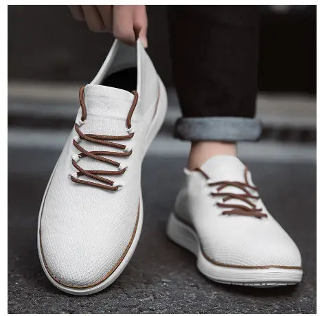 Men’s flyknit casual breathable lace up sneakers in white canvas with brown laces and matching stitched trim along the sole.
