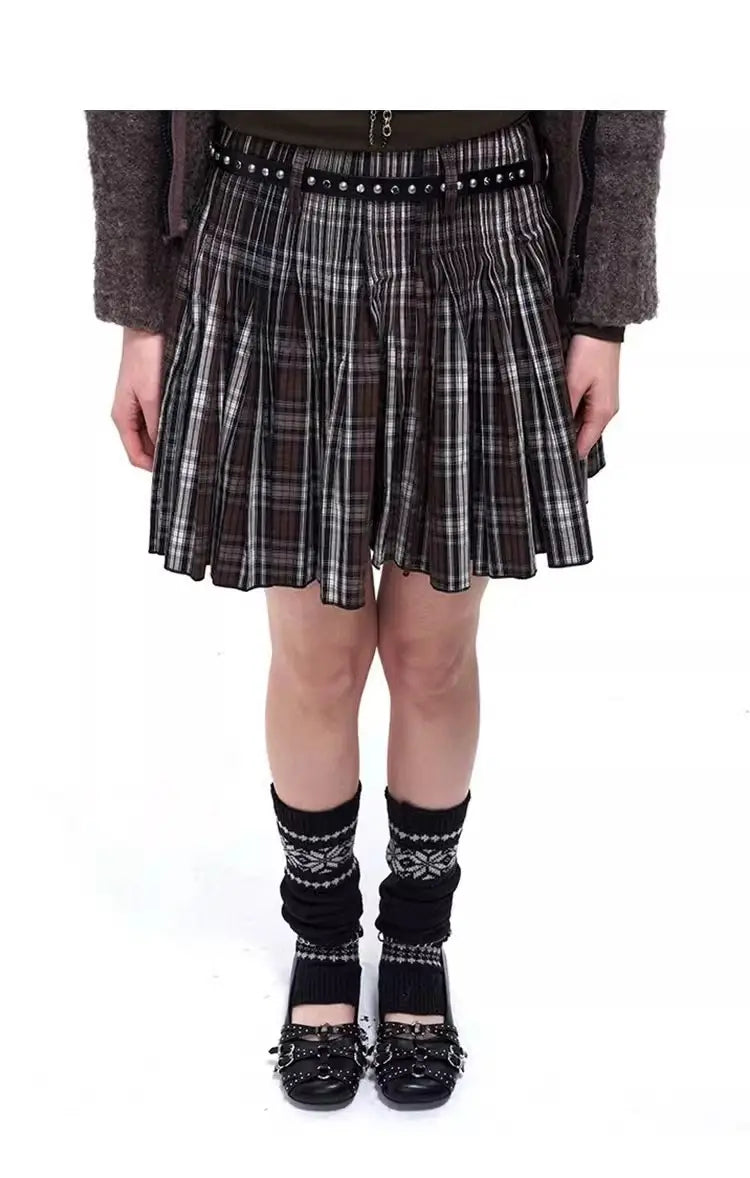 falda plisada de cuadros en blanco y negro con cinturón con tachuelas, combinada con zapatos tipo salón retro de cuero con correas de hebilla con tachuelas