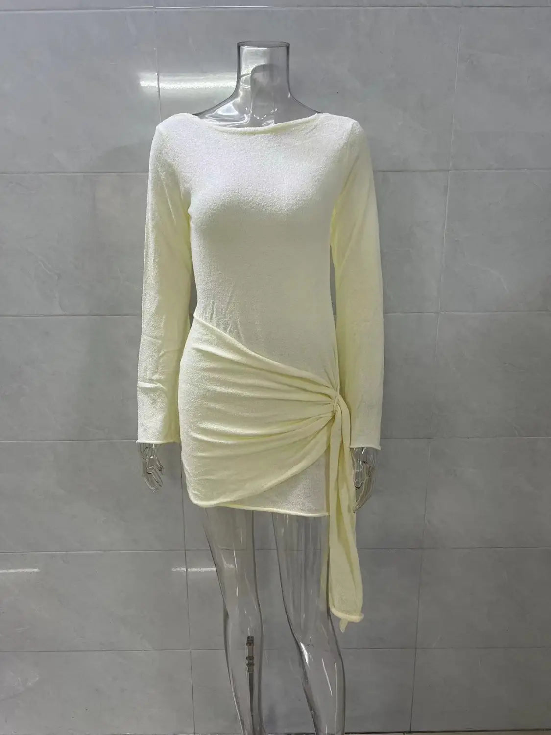 A pale yellow backless long sleeve knit mini dress with a draped side tie detail.