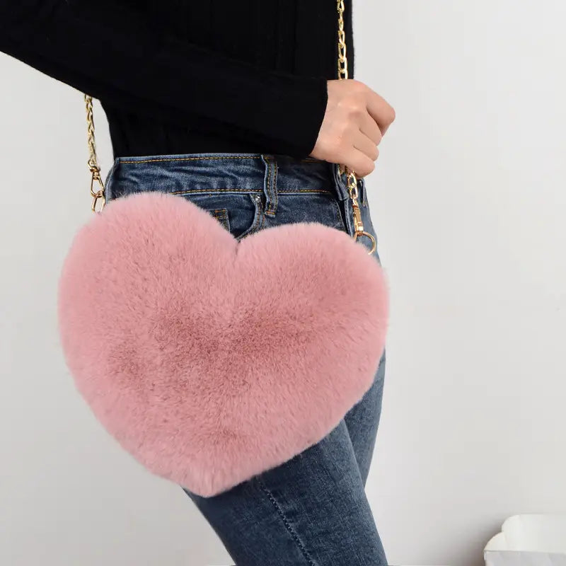 Plush faux fur heart shaped crossbody bag in pink with a gold chain strap.