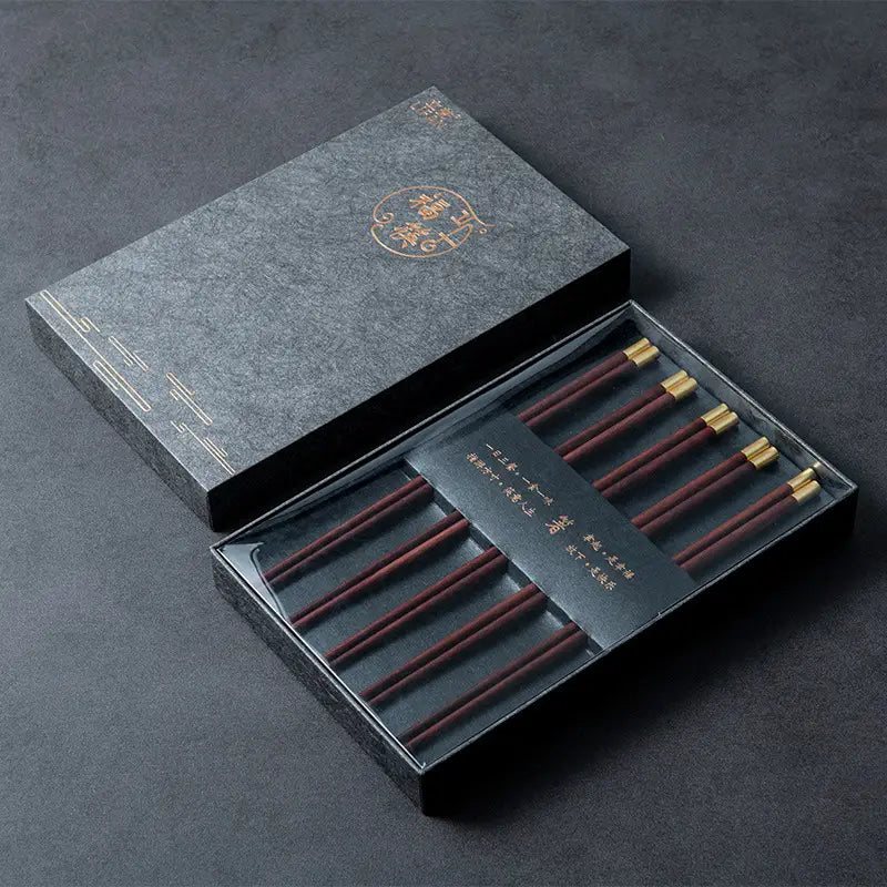 Set aus sechs dunkelroten hölzernen Essstäbchen mit goldfarbenen Spitzen, in einer eleganten schwarzen Geschenkbox präsentiert, für ein Essstäbchen-Set mit goldfarbenen Spitzen, 5 Paar Geschenkbox.