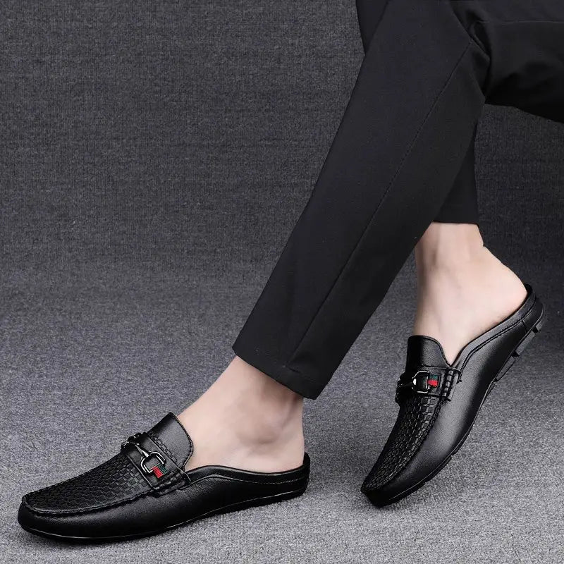 Men’s black leather mule loafers featuring a textured pattern and a red and black woven buckle accent.
