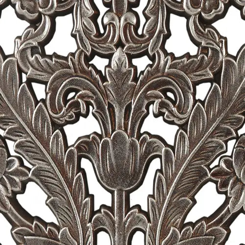Antique-style metal trivet with intricate floral and leaf patterns in a dark aged bronze finish complementing carved wood wall decor set distressed botanical panels.