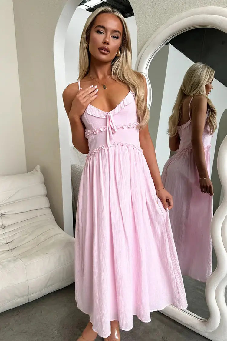 A soft pink flowing midi dress with delicate ruffled detailing at the neckline and waist designed as a ruffled sleeveless flowing maxi vacation dress.