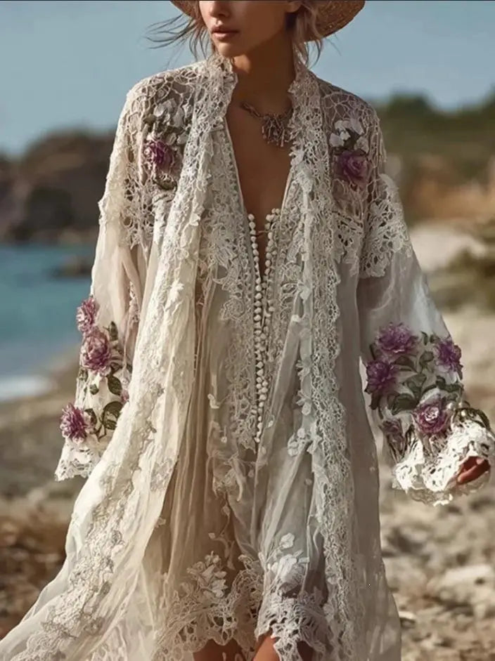 Ein fließendes Vintage-Midikleid mit langen Ärmeln aus off-whitefarbener Spitze als Strandüberwurf mit aufwendiger violetter und grüner Blumenstickerei sowie zarten Durchbruchdetails an den Ärmeln und am Saum.