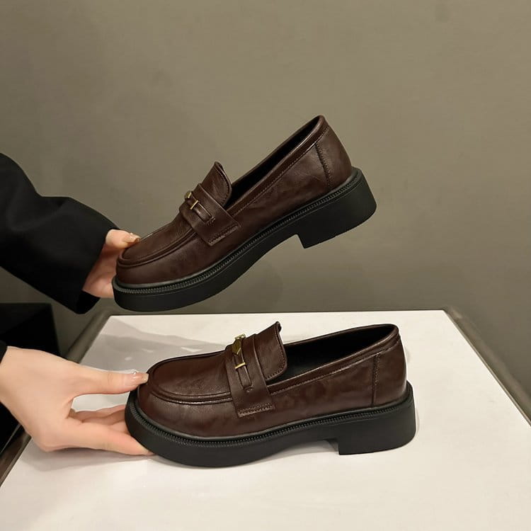 Brown leather loafers with a thick black rubber sole and gold-tone metal buckle detail.