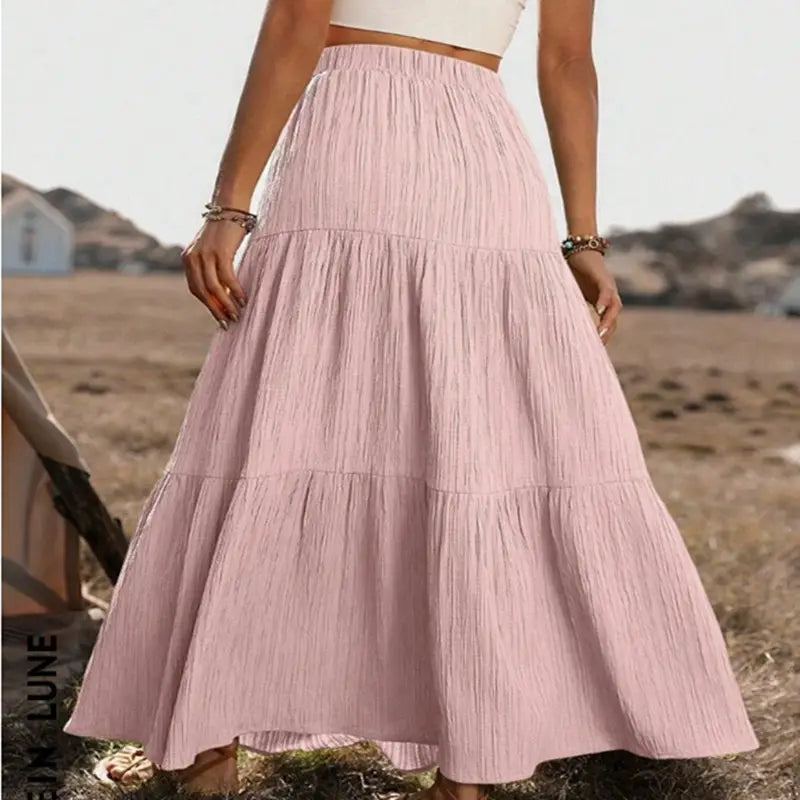 A flowing light pink tiered maxi skirt with a gathered waist subtle vertical pleats and button front detail, lightweight and suitable for casual wear.