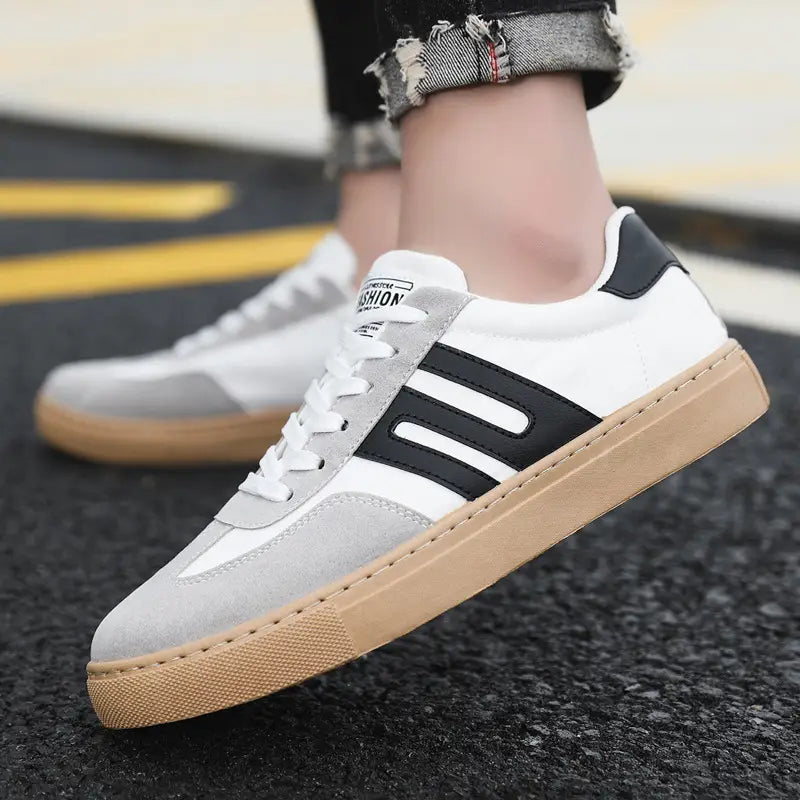 Chaussures de planche de mode décontractées en daim pour homme à tige basse, en blanc et gris, avec des bandes noires et une semelle en caoutchouc tan, comportant un petit logo de mode sur la languette.