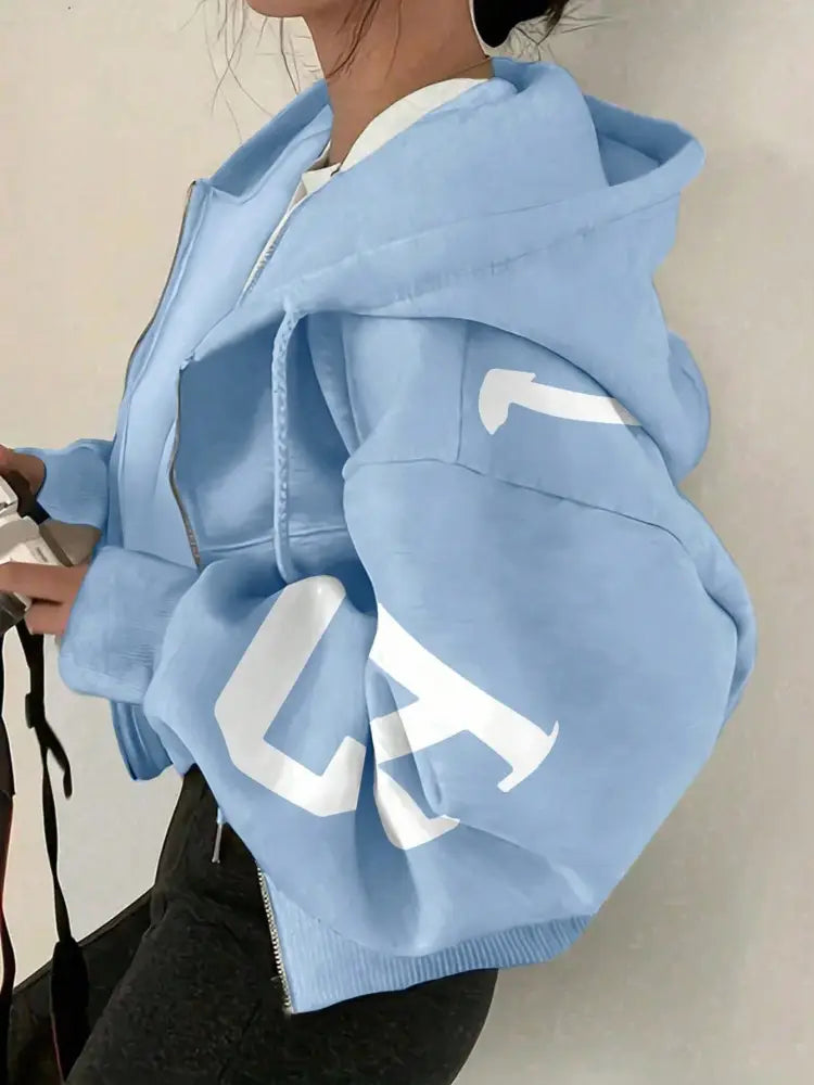 Sweat-shirt à capuche zippé imprimé graphique bleu clair, avec un lettrage blanc audacieux sur les manches.