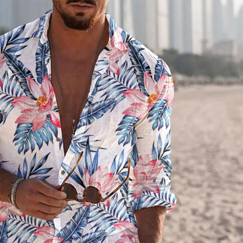 Ein Mann, der ein weißes Hemd mit blau-rosa tropischem Print und langem Ärmel für Herren am Strand trägt, mit hochgekrempelten Ärmeln.