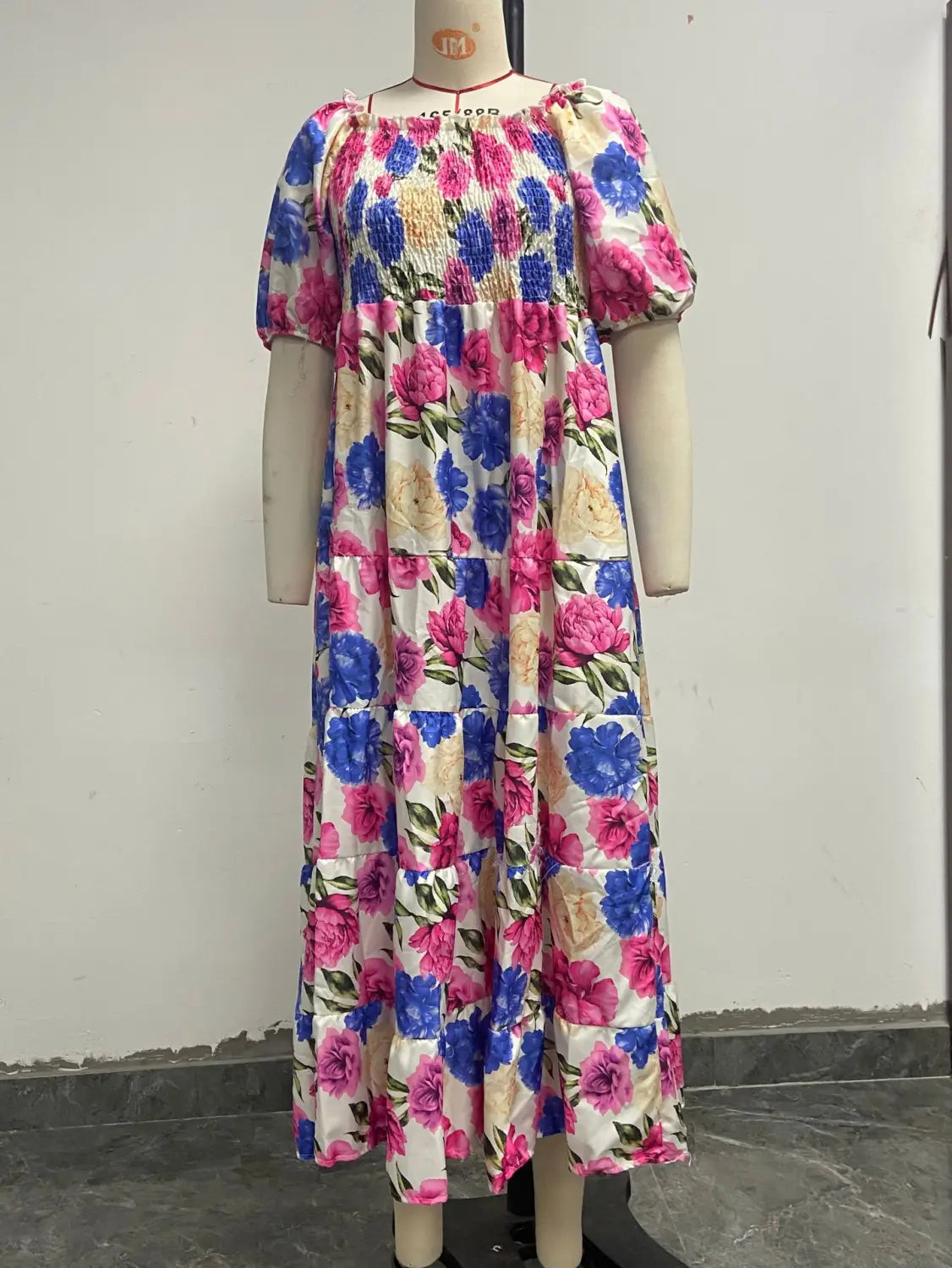 Floral print smocked tiered midi dress with square neckline featuring a vibrant cream background with bold pink and blue blossoms and puffy short sleeves.