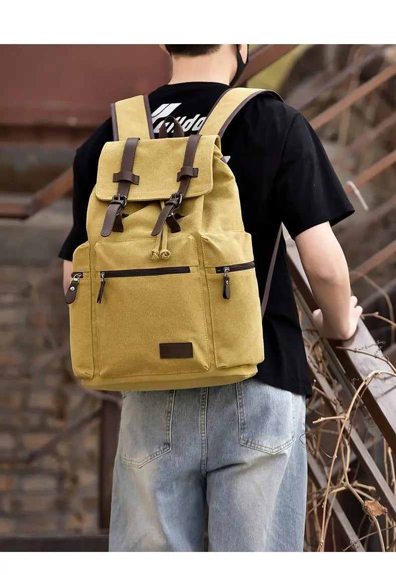A mustard yellow canvas men’s travel backpack with brown leather straps and accents featuring a large 20-35 liter capacity.