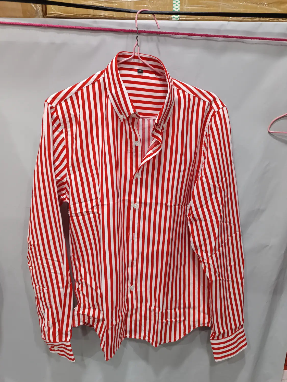 Herren gestreiftes Slim-Fit-Langarm-Freizeithemd in rot-weißen vertikalen Streifen, das an einem rosa Bügel hängt.