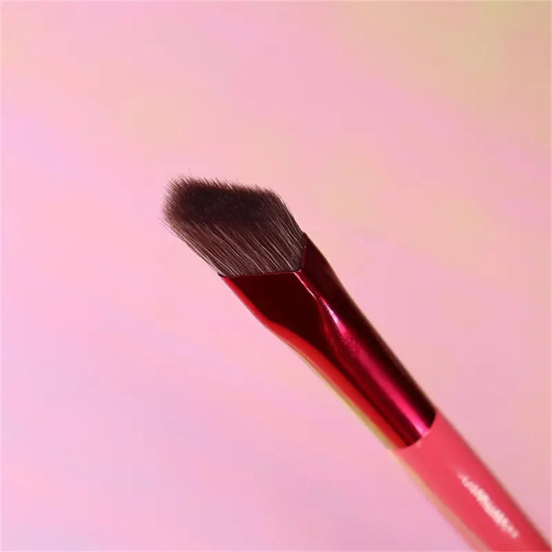 A sleek red-handled angled eyebrow and concealer makeup brush with a dense black bristle head for precise application.