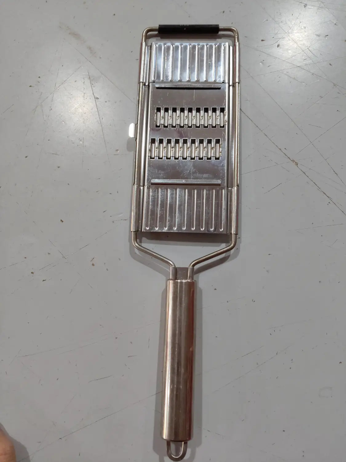 Juego de rallador y cortador multiusos de acero inoxidable con asa de plástico negro y tres superficies de corte diferenciadas para una preparación versátil de verduras.