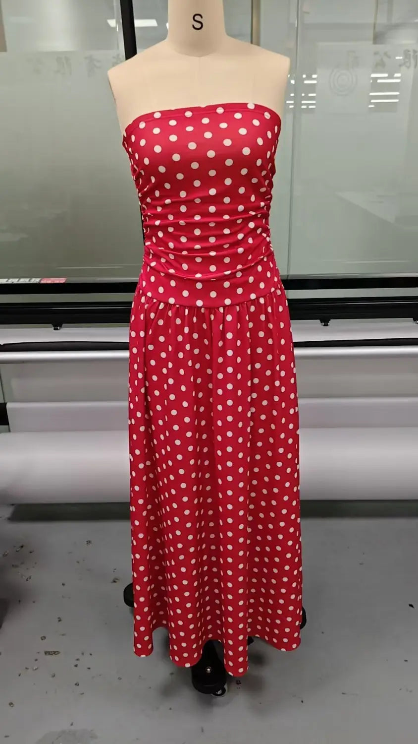 A vibrant red strapless maxi dress with white polka dots made from flowing fabric designed for elegant occasions.