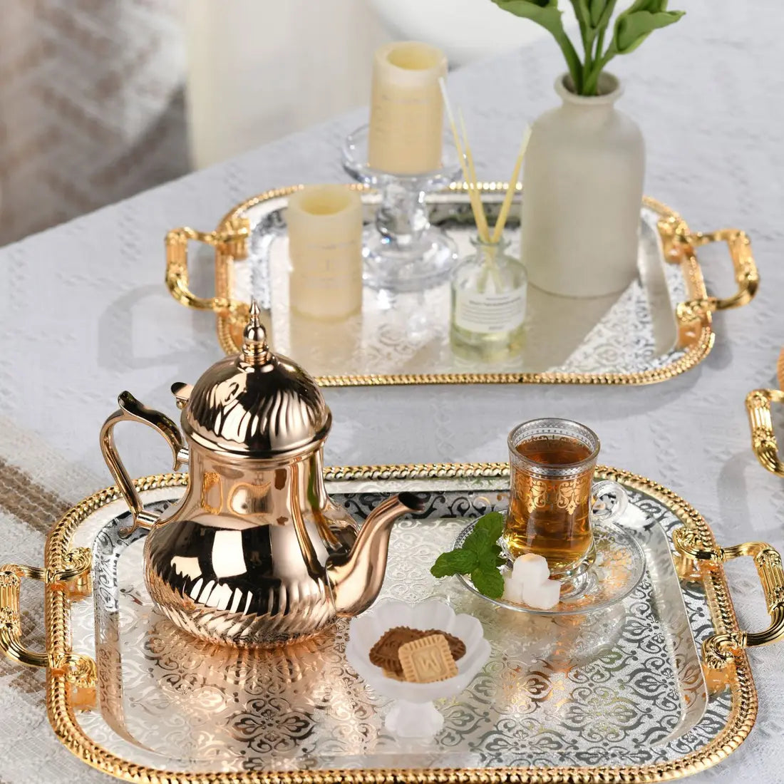 Luxury rectangle serving tray with gold handles displaying a golden ornate teapot with a ribbed body and decorative lid resting on an intricately patterned surface.