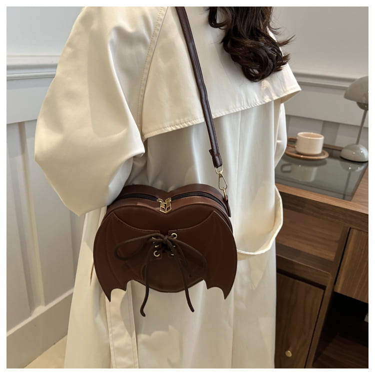Brown bat-shaped crossbody bag with lace-up front detail and gold-tone hardware designed for stylish everyday use.