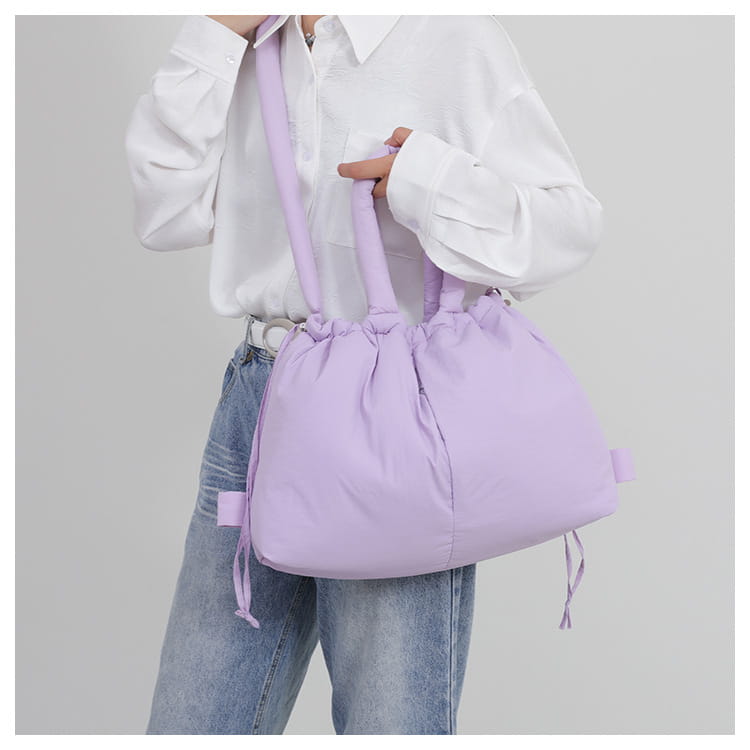 A soft lavender quilted puffer tote bag made of lightweight nylon featuring a padded design and matching drawstring shoulder strap.