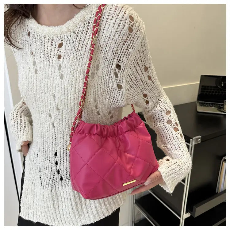Fuchsia quilted faux leather crossbody bag with satin texture and pink chain strap for stylish carrying.