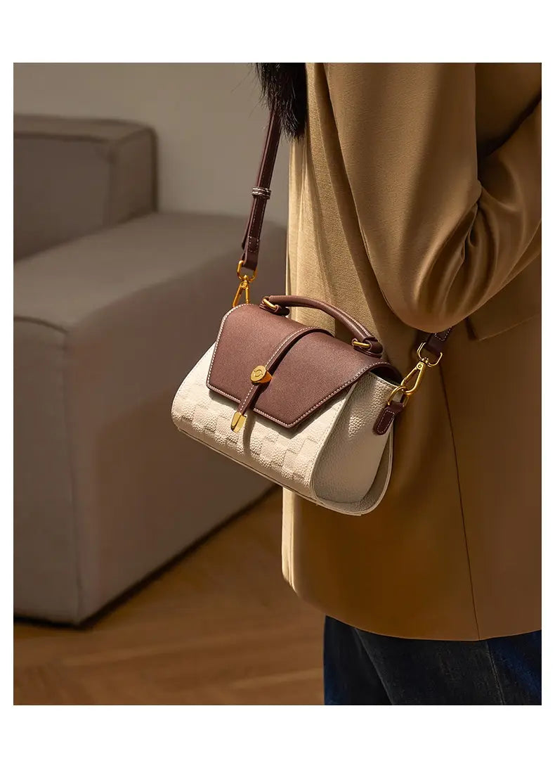 Eine zweifarbige Webleder-Crossbody-Handtasche mit beigem, strukturiertem Körper, braunem Leder-Flip und Griffen, goldfarbenen Beschlägen und verstellbarem Crossbody-Gurt.