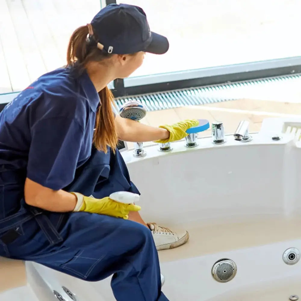 A woman in navy uniform cleaning a white whirlpool tub equipped with a non-slip silicone suction bath mat
