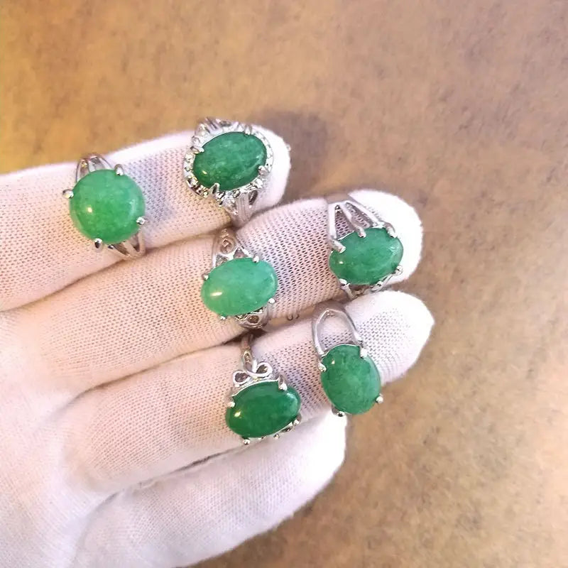 A hand wearing a white glove holds five elegant natural gemstone silver tone statement rings featuring oval-shaped green jade gemstones set in intricate filigree metalwork.